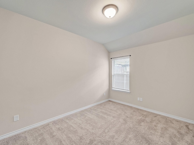 carpeted spare room featuring baseboards and vaulted ceiling