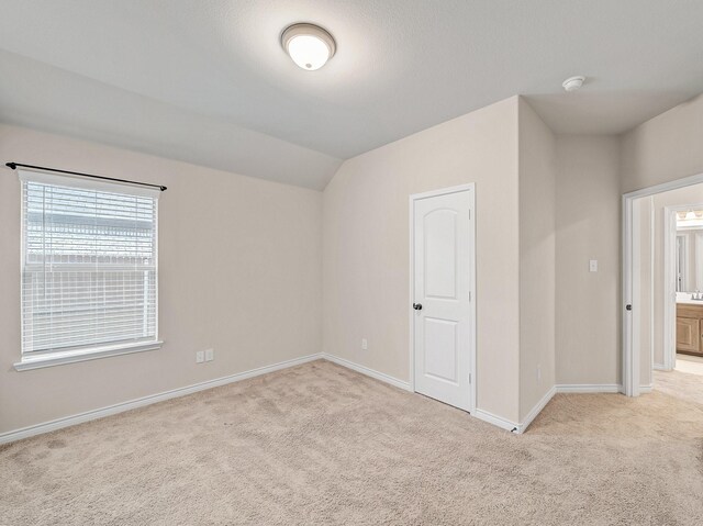 empty room featuring light colored carpet, baseboards, and vaulted ceiling