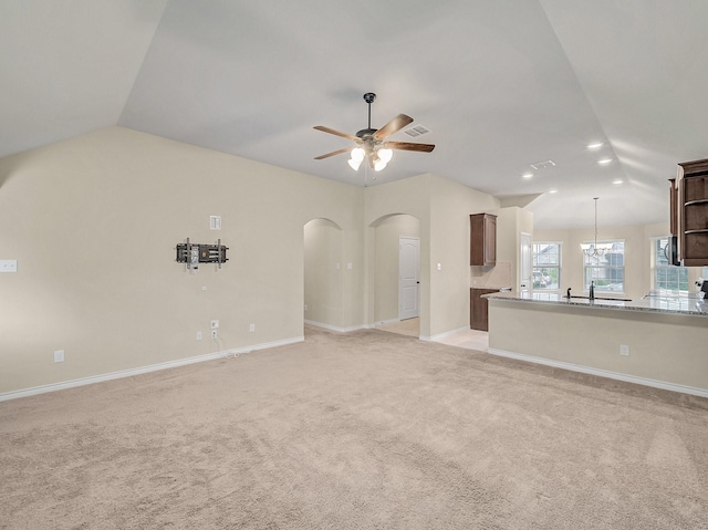 unfurnished living room featuring light colored carpet, vaulted ceiling, a ceiling fan, and arched walkways