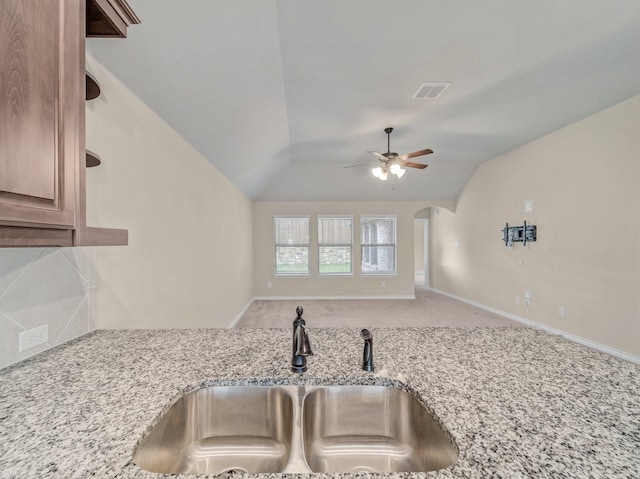 kitchen with visible vents, a sink, arched walkways, light stone countertops, and vaulted ceiling