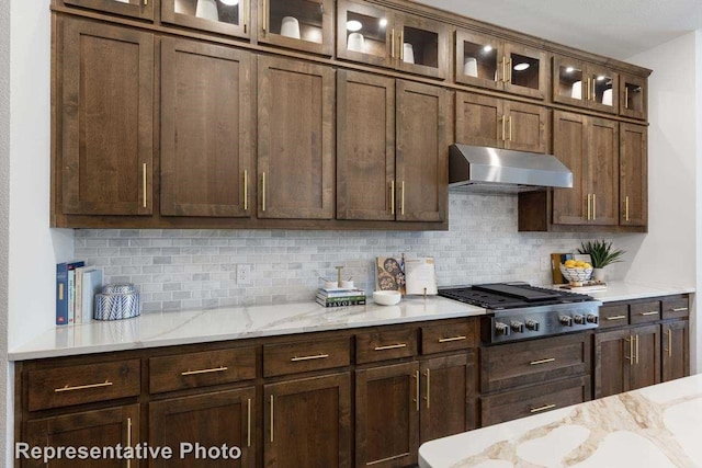 1409 Roundwash Way, Midlothian, TX 76065 - kitchen with under cabinet range hood, stainless steel gas cooktop, decorative backsplash, light stone counters, and glass insert cabinets