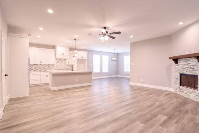 unfurnished living room with light wood-type flooring, baseboards, ceiling fan, and a fireplace