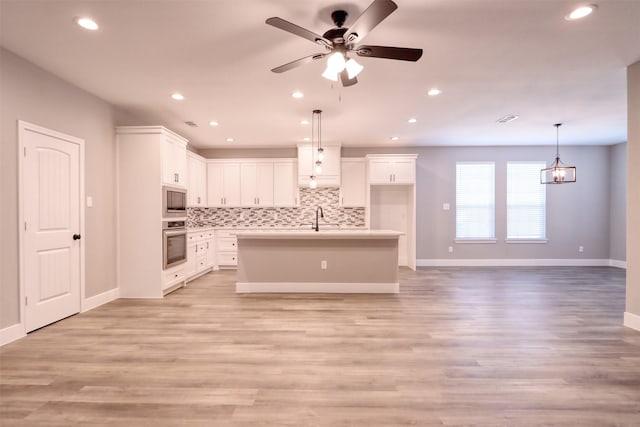 kitchen with tasteful backsplash, appliances with stainless steel finishes, light wood-style flooring, and white cabinetry