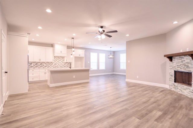 unfurnished living room with baseboards, a fireplace, light wood-style flooring, and a ceiling fan