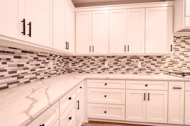 kitchen featuring tasteful backsplash, white cabinets, light stone countertops, and stainless steel gas stovetop