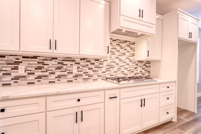 kitchen with tasteful backsplash, light stone countertops, light wood-type flooring, stainless steel gas stovetop, and white cabinetry