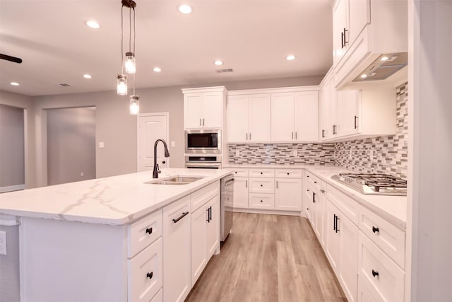 kitchen featuring light wood finished floors, decorative backsplash, appliances with stainless steel finishes, and a sink