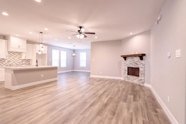 unfurnished living room featuring a stone fireplace, baseboards, light wood-type flooring, and ceiling fan