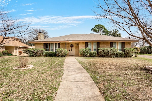 ranch-style home featuring a front yard, brick siding, a chimney, and a shingled roof