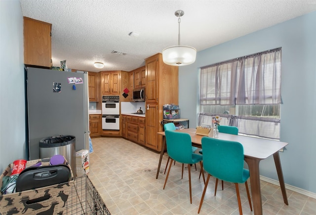 kitchen with brown cabinetry, visible vents, stainless steel appliances, light countertops, and a textured ceiling