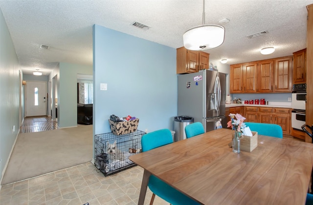 kitchen featuring visible vents, double oven, light countertops, and stainless steel refrigerator with ice dispenser