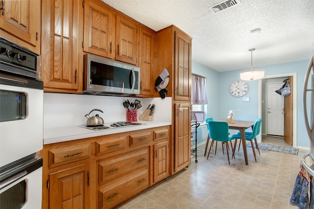 kitchen featuring visible vents, brown cabinets, white appliances, light countertops, and hanging light fixtures