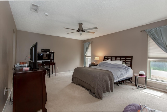 carpeted bedroom with visible vents, a textured ceiling, baseboards, and a ceiling fan