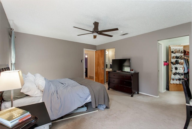 bedroom with visible vents, ceiling fan, a textured ceiling, a walk in closet, and light colored carpet