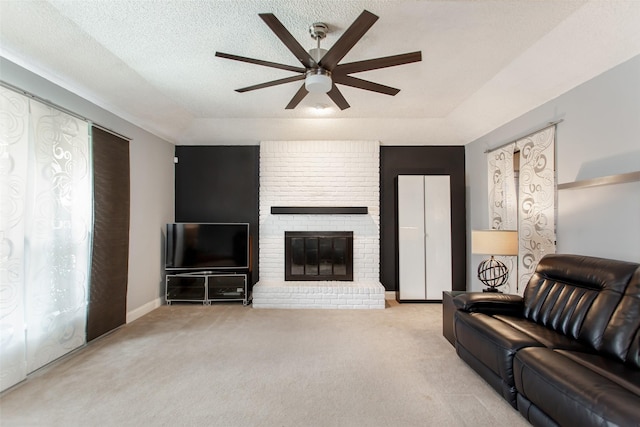 living area with a brick fireplace, carpet flooring, a textured ceiling, a raised ceiling, and a ceiling fan