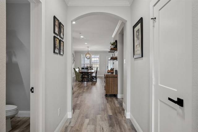 hallway with baseboards, ornamental molding, recessed lighting, wood finished floors, and arched walkways