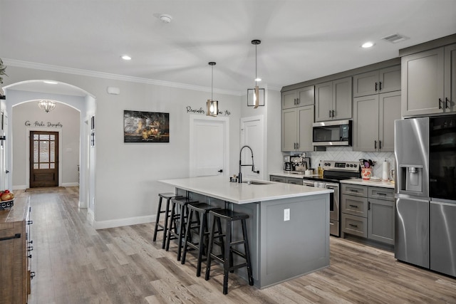 kitchen featuring arched walkways, ornamental molding, gray cabinetry, a sink, and appliances with stainless steel finishes