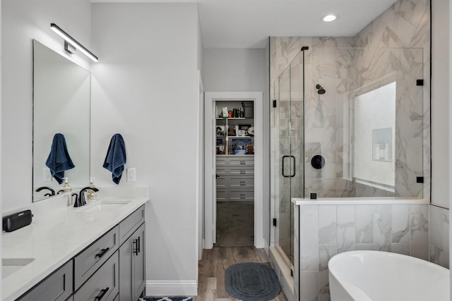 full bath with a sink, wood finished floors, a shower stall, double vanity, and a soaking tub