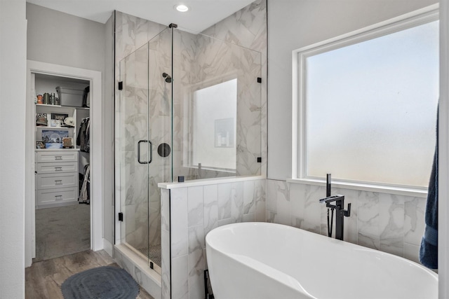 full bathroom featuring wood finished floors, recessed lighting, a marble finish shower, a soaking tub, and a spacious closet