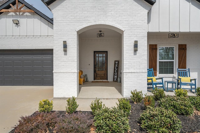 doorway to property with brick siding, a porch, an attached garage, and board and batten siding