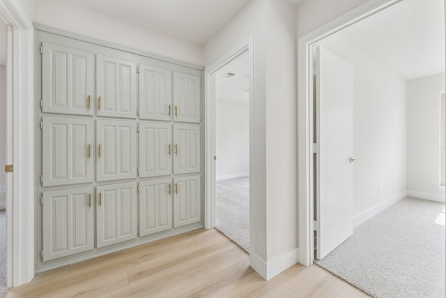 hall featuring visible vents, light wood-style floors, light colored carpet, and baseboards