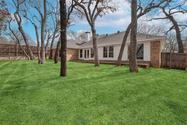 rear view of house with brick siding, a chimney, a yard, and fence