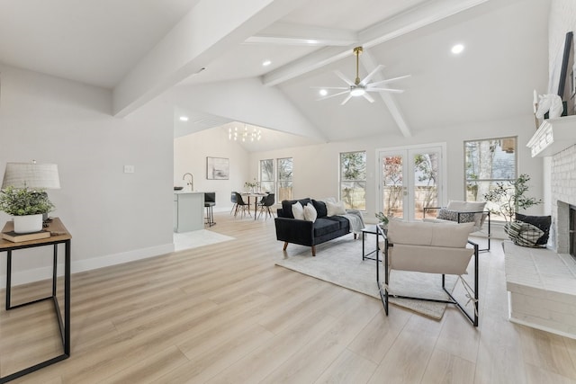 living area with a brick fireplace, baseboards, beamed ceiling, light wood-style flooring, and french doors