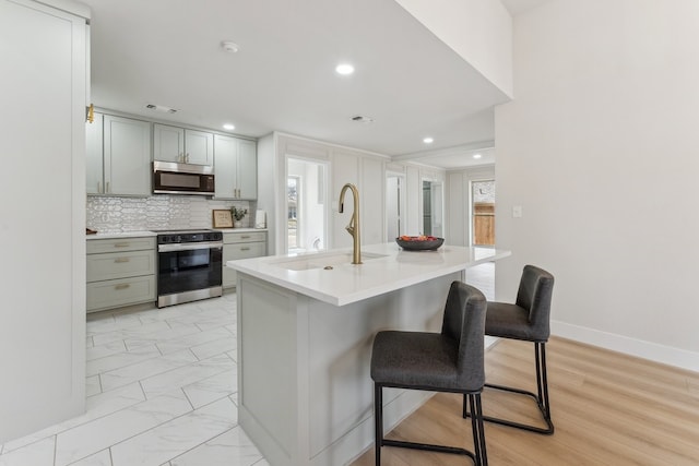 kitchen featuring visible vents, decorative backsplash, appliances with stainless steel finishes, a kitchen breakfast bar, and a sink