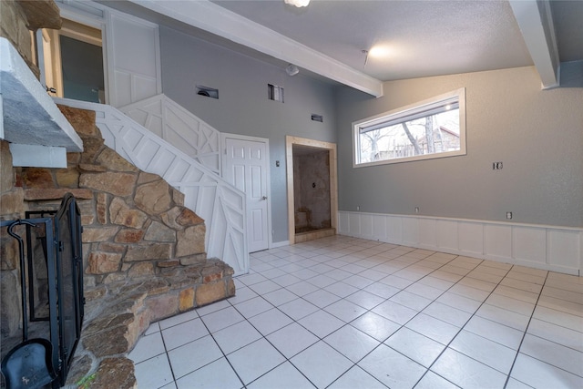 unfurnished living room featuring light tile patterned floors, a decorative wall, wainscoting, and lofted ceiling with beams