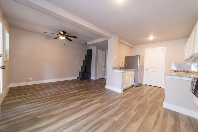 unfurnished living room featuring a sink, light wood-style flooring, baseboards, and ceiling fan