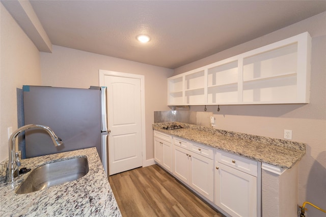 kitchen with a sink, light stone counters, wood finished floors, white cabinets, and open shelves