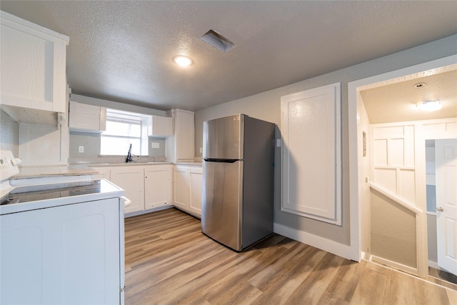 kitchen with white range with electric cooktop, light wood-style flooring, white cabinets, and freestanding refrigerator