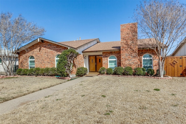 ranch-style house featuring brick siding, a chimney, a front yard, and roof with shingles