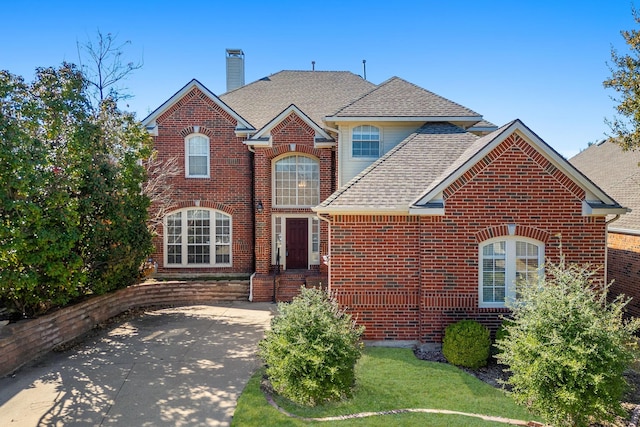 traditional-style home with brick siding, a chimney, and a shingled roof