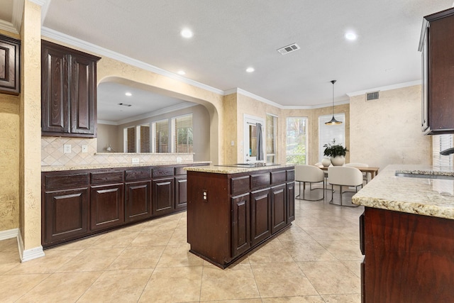 kitchen featuring visible vents, a kitchen island, a sink, decorative backsplash, and crown molding