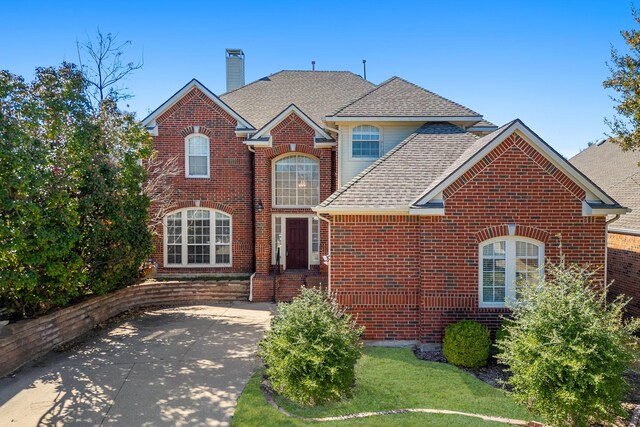 traditional-style home featuring driveway, a shingled roof, a garage, brick siding, and a chimney