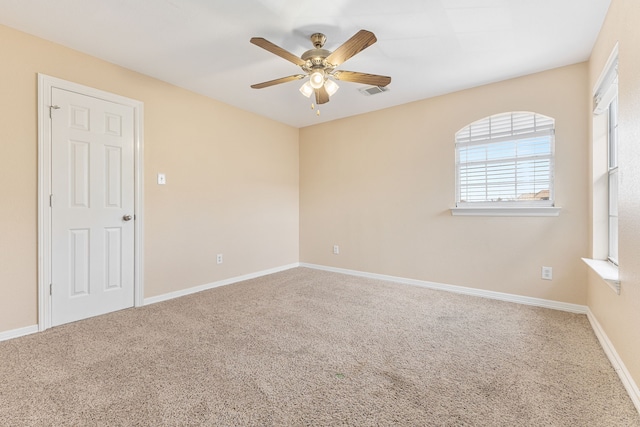 carpeted spare room with visible vents, baseboards, and a ceiling fan