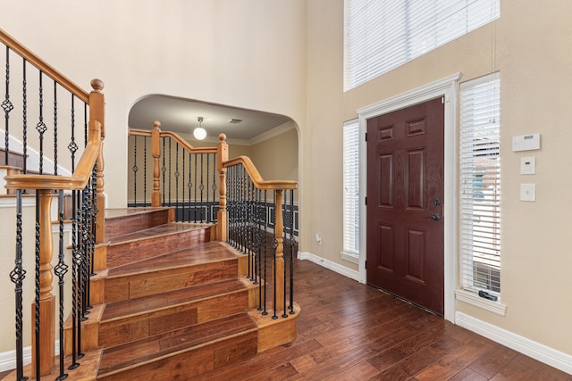 entrance foyer with arched walkways, stairs, a wealth of natural light, and hardwood / wood-style floors