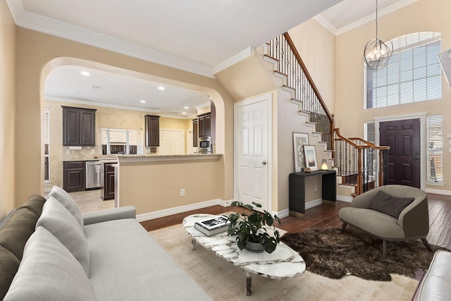 living area featuring ornamental molding, wood finished floors, arched walkways, a chandelier, and stairs