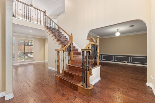 staircase with visible vents, ornamental molding, a towering ceiling, arched walkways, and wood-type flooring