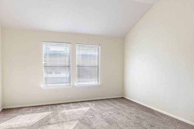 carpeted spare room featuring baseboards and vaulted ceiling