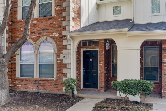 doorway to property featuring brick siding, board and batten siding, and a shingled roof