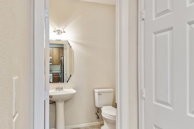 half bath with toilet, baseboards, and a sink