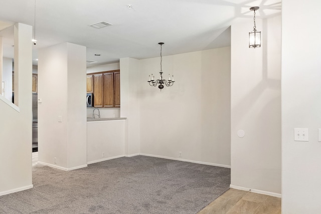 unfurnished dining area featuring a notable chandelier, baseboards, visible vents, and light carpet