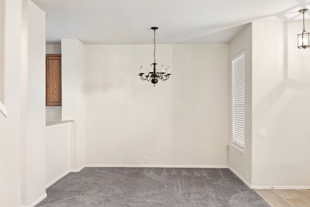 unfurnished dining area featuring a notable chandelier, light colored carpet, and baseboards