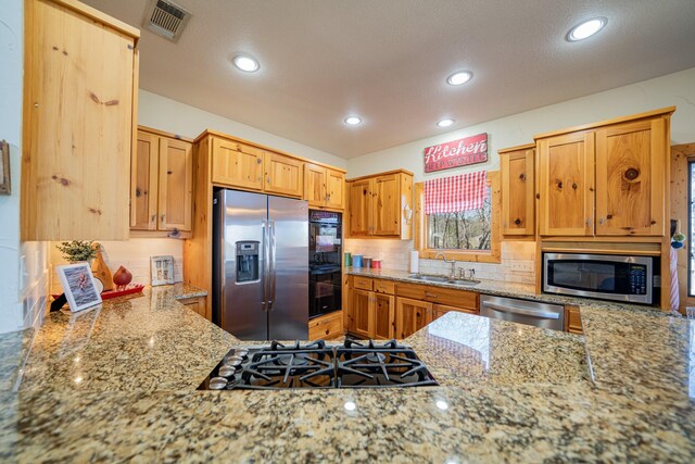 kitchen featuring visible vents, backsplash, light stone counters, appliances with stainless steel finishes, and a sink