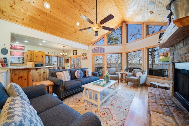 living area with light wood finished floors, wood ceiling, ceiling fan with notable chandelier, a fireplace, and high vaulted ceiling