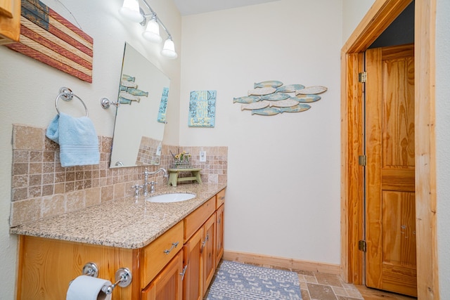 bathroom featuring decorative backsplash, baseboards, vanity, and stone finish floor