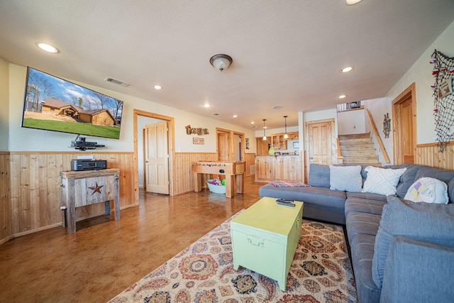 living area featuring visible vents, a textured ceiling, a wainscoted wall, and stairs