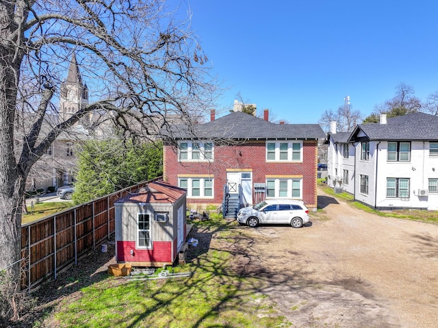 rear view of property with brick siding, fence, a residential view, a storage shed, and an outbuilding